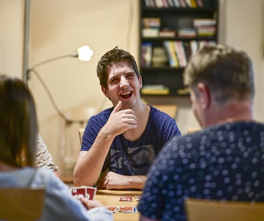 Drei Menschen sitzen am Tisch und spielen gut gelaunt arten