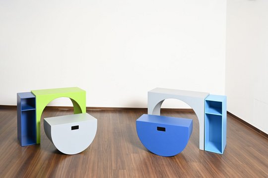 Zwei bunte, geometrische Möbelstücke auf Holzboden vor weißer Wand.