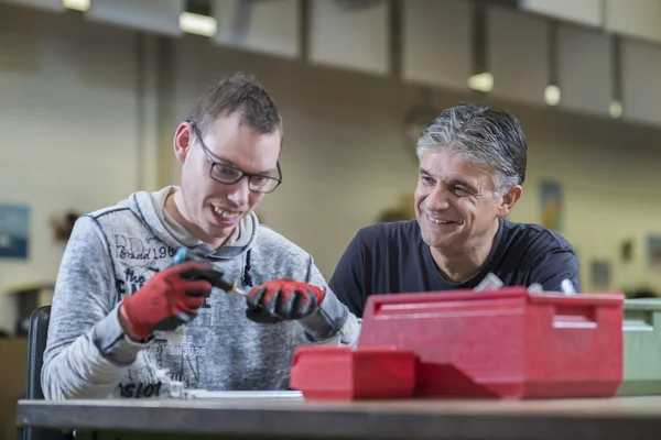 Zwei Männer arbeiten lächelnd an einem Tisch in einer Werkstatt.