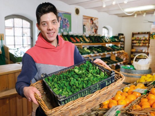 Mann hält Korb mit frischem Gemüse in einem Lebensmittelladen.
