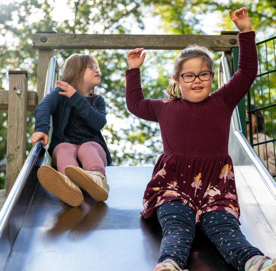 Zwei Kinder rutschen fröhlich eine Rutsche hinunter im Park.