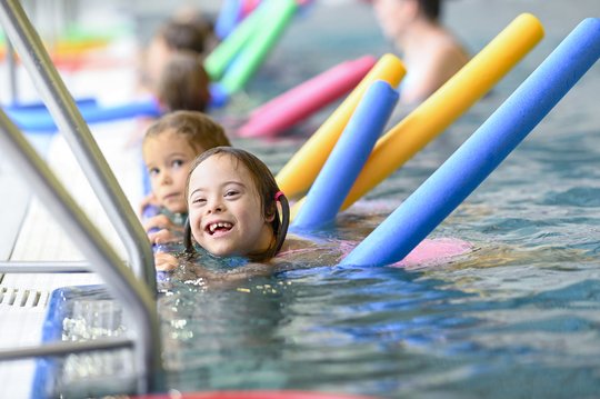Kinderschwimmkurs, bei dem die Teilnehmenden mit bunten Poolnudeln schwimmen