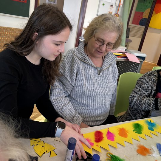 Zwei Frauen basteln gemeinsam mit bunten Federn an einem Tisch.