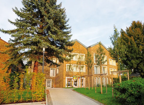 Mehrstöckiges Backsteingebäude mit Bäumen und Pflasterweg.
