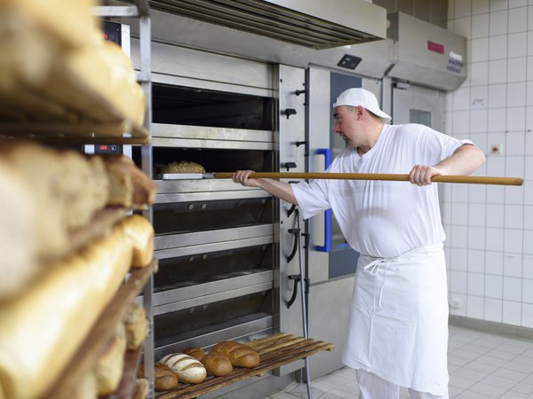 Bäckereimitarbeiter holt Brot aus dem Ofen