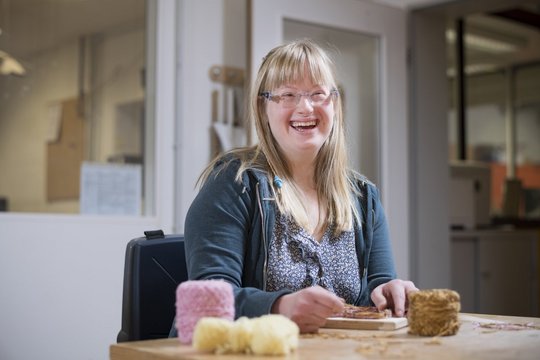 Lachende Teilnehmerin des Berufsbildungsbereichs probiert ihre Feinmotorik bei einer Aufgabe aus.