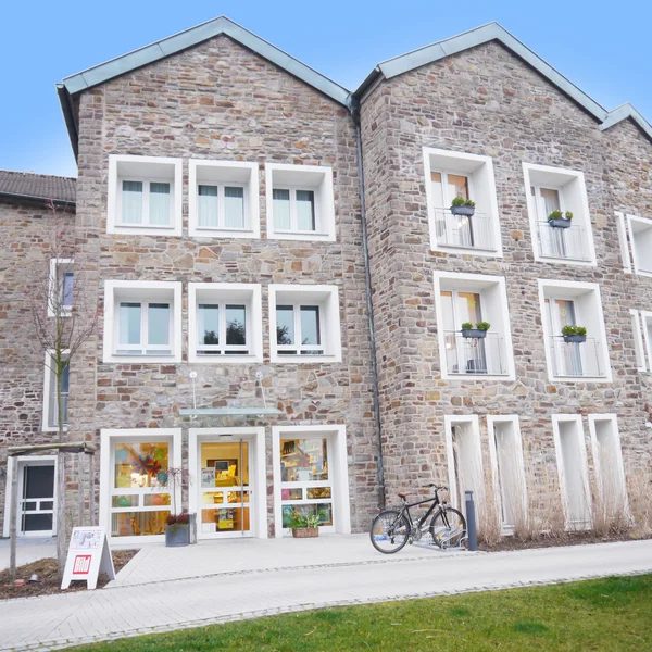 Steingebäude mit Fenstern, Fahrrad vor Eingang, blauer Himmel.