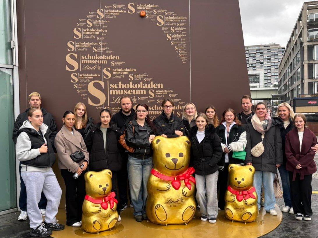 Die Klasse steht vor dem Kölner Schokoladenmuseum. Sie umringen 3 große goldene Figuren der bekannten Lindt-Schokobären