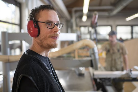 Beschäftigter mit Gehörschutz an einer Maschine in der Schreinerei