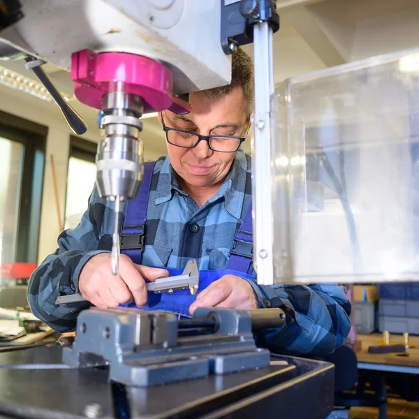 Person arbeitet konzentriert an einer Bohrmaschine in einer Werkstatt.