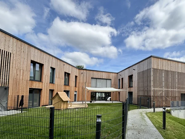 Modernes Gebäude mit Holzfassade und eingezäuntem Garten bei bewölktem Himmel.