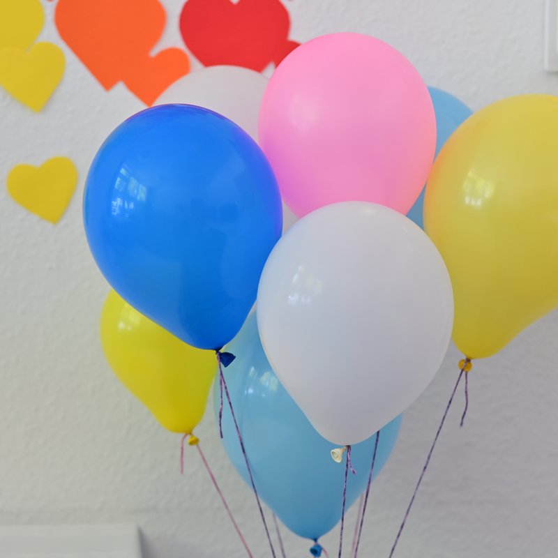 Bunte Luftballons vor einer weißen Wand, dekoriert mit bunten Herzen.