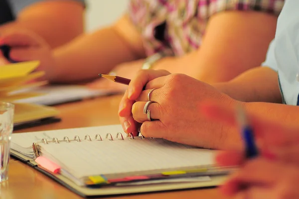 Person schreibt mit Stift in ein Notizbuch bei einem Treffen.