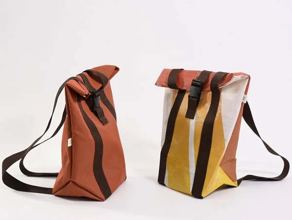 Zwei bunte Rucksäcke mit Streifen und schwarzen Gurten auf hellem Hintergrund.