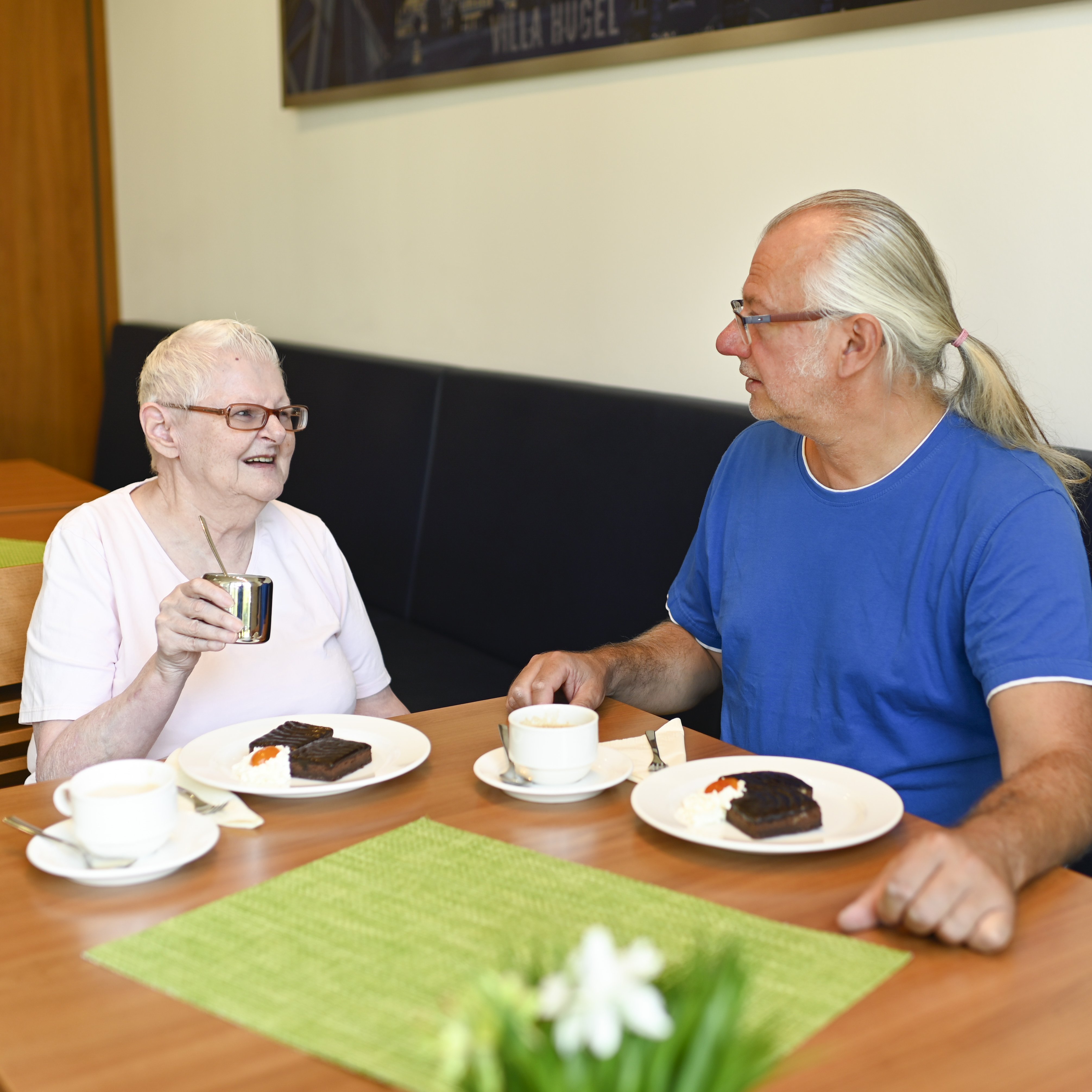 Klientin und Ehrenamtlicher trinken Kaffee und essen Kuchen an einem Tisch in einem Café.