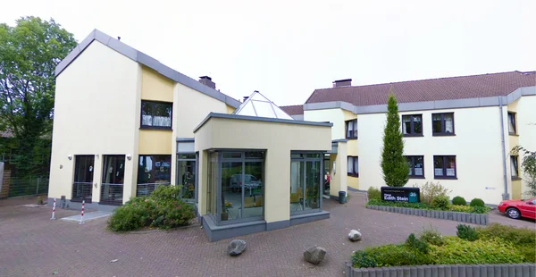 Modernes Gebäude mit beige Fassade, Glasfront und Dachvorsprung in einer grünen Umgebung.