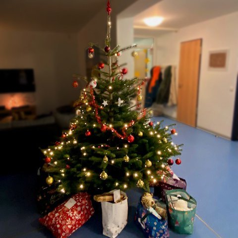 Beleuchteter Weihnachtsbaum mit Geschenken darunter in einem Wohnzimmer.