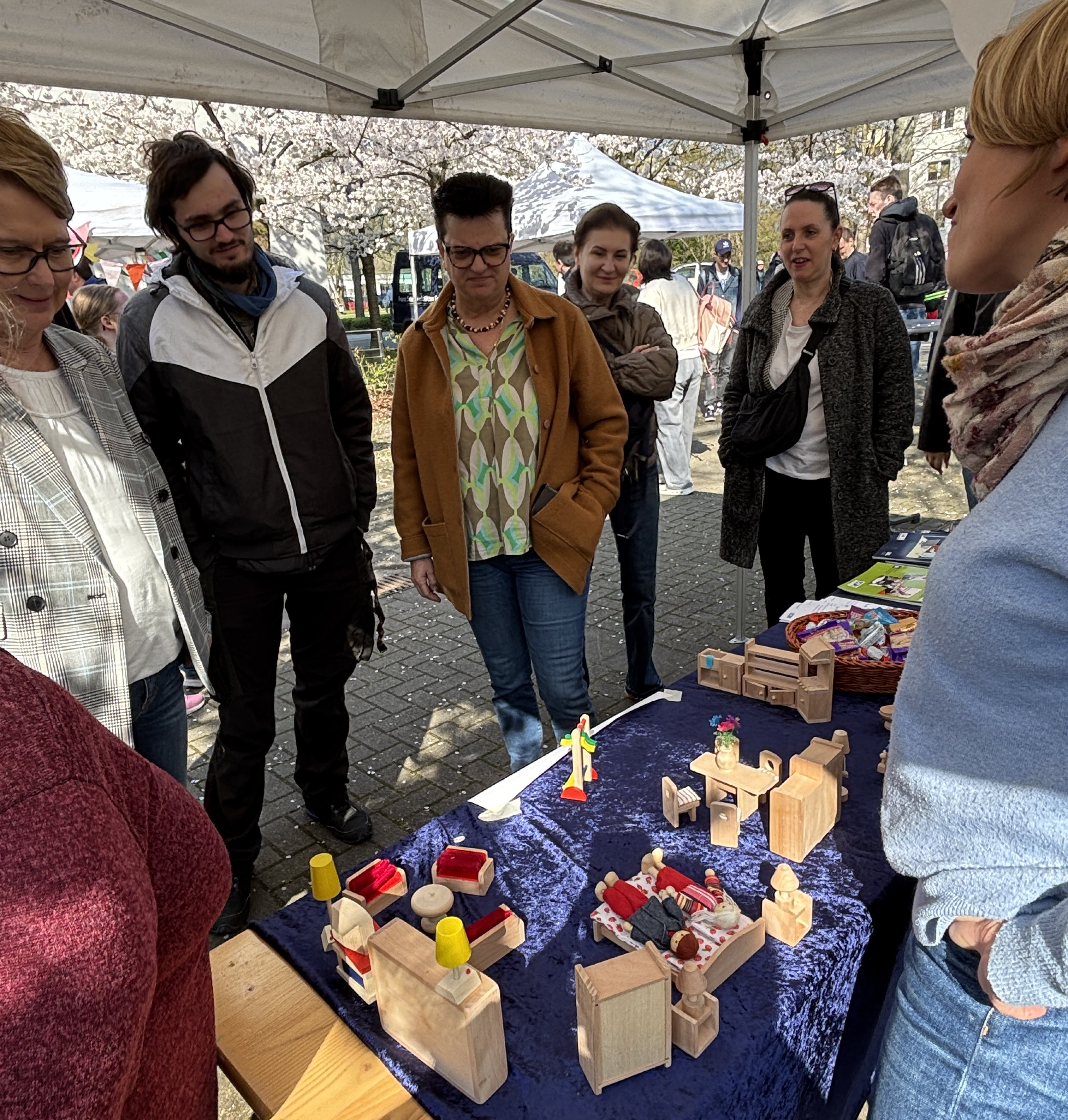 An einem Infostand gibt es auf einem Tisch Flyer und kleine Möbel aus Holz. Ein junger Mann baut mit den Möbeln seine Wunsch-Wohnung auf.