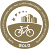 Siegel „Fahrradfreundlicher Arbeitgeber“, Gold, mit Fahrrad und Gebäuden.