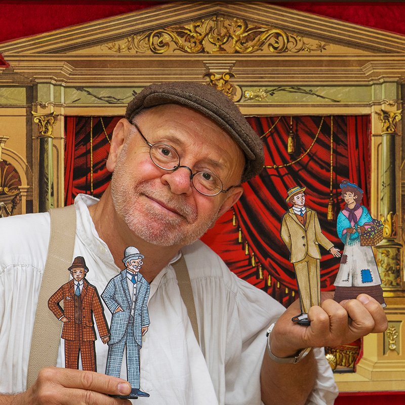 Mann mit Flachfiguren vor einer Miniatur-Bühne in traditioneller Kulisse.