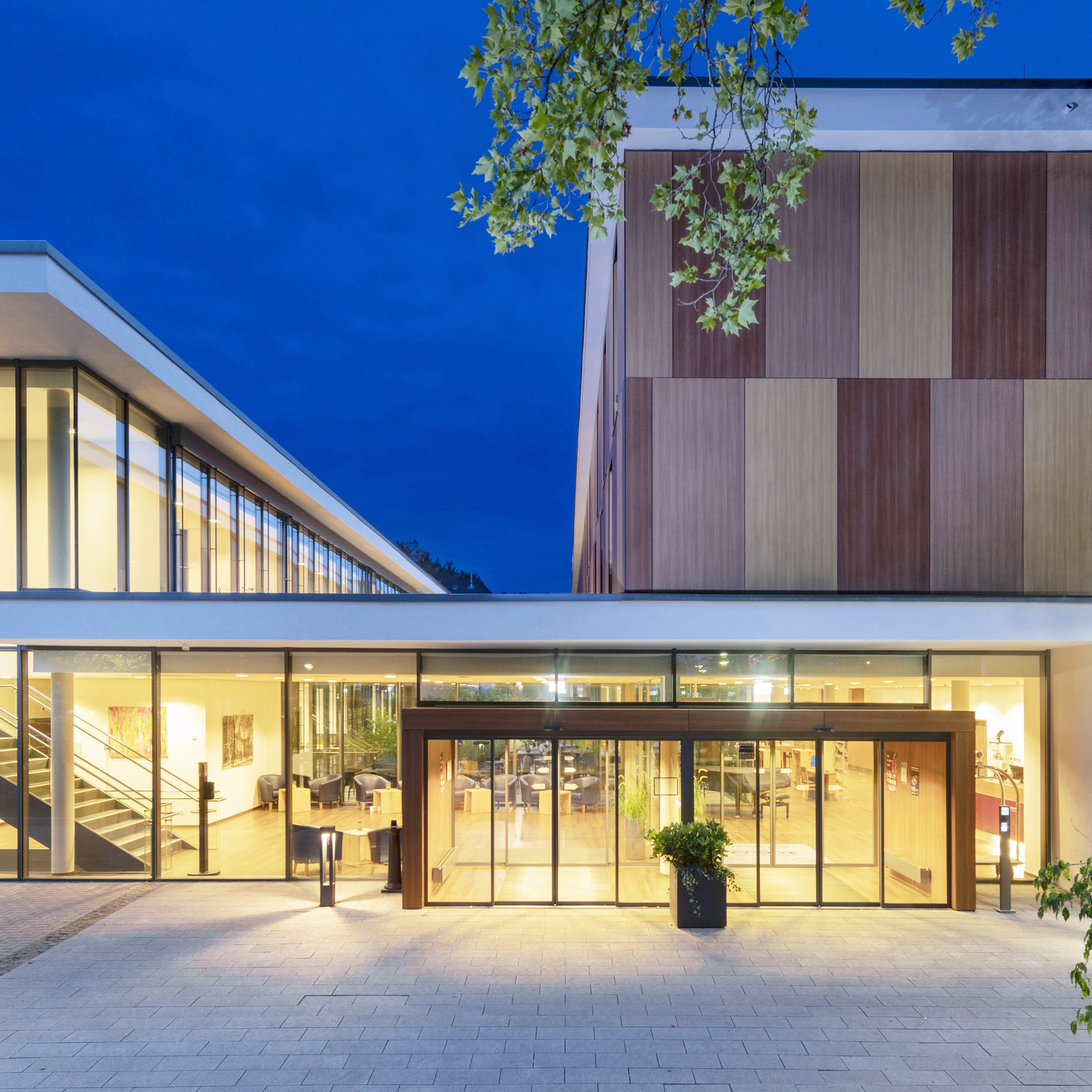 Modernes Gebäude des Hotels Franz in Essen mit Glasfronten bei Nacht, beleuchtet und von Bäumen umgeben.