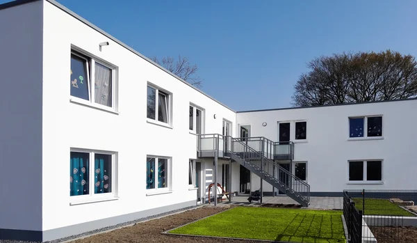 Modernes zweistöckiges Gebäude mit weißer Fassade und Außentreppe.