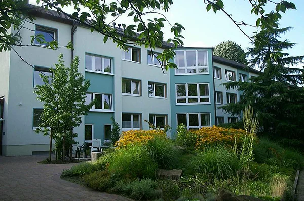 Mehrstöckiges Gebäude mit grüner Fassade, umgeben von Bäumen und Büschen.