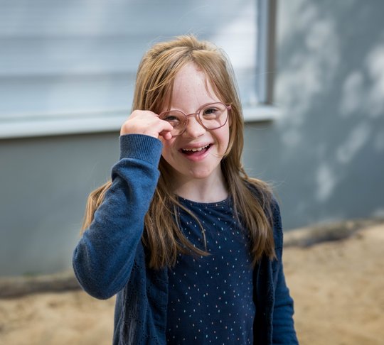Ein lächelndes Mädchen mit Brille und blauer Kleidung im Freien.