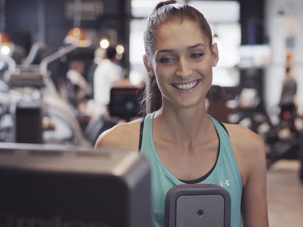 lächelnde Sportlerin auf einem Milon-Fitnessgerät im Fitnessstudio.