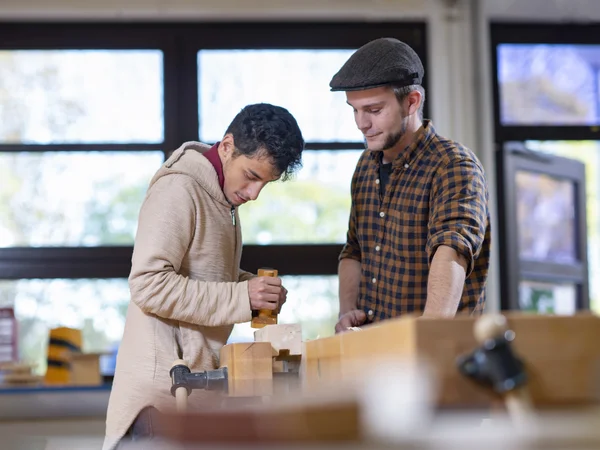 Teilnehmer des Berufsbildungsbereichs mit Hobel wird von einem Schreiner an der Hobelbank angeleitet.