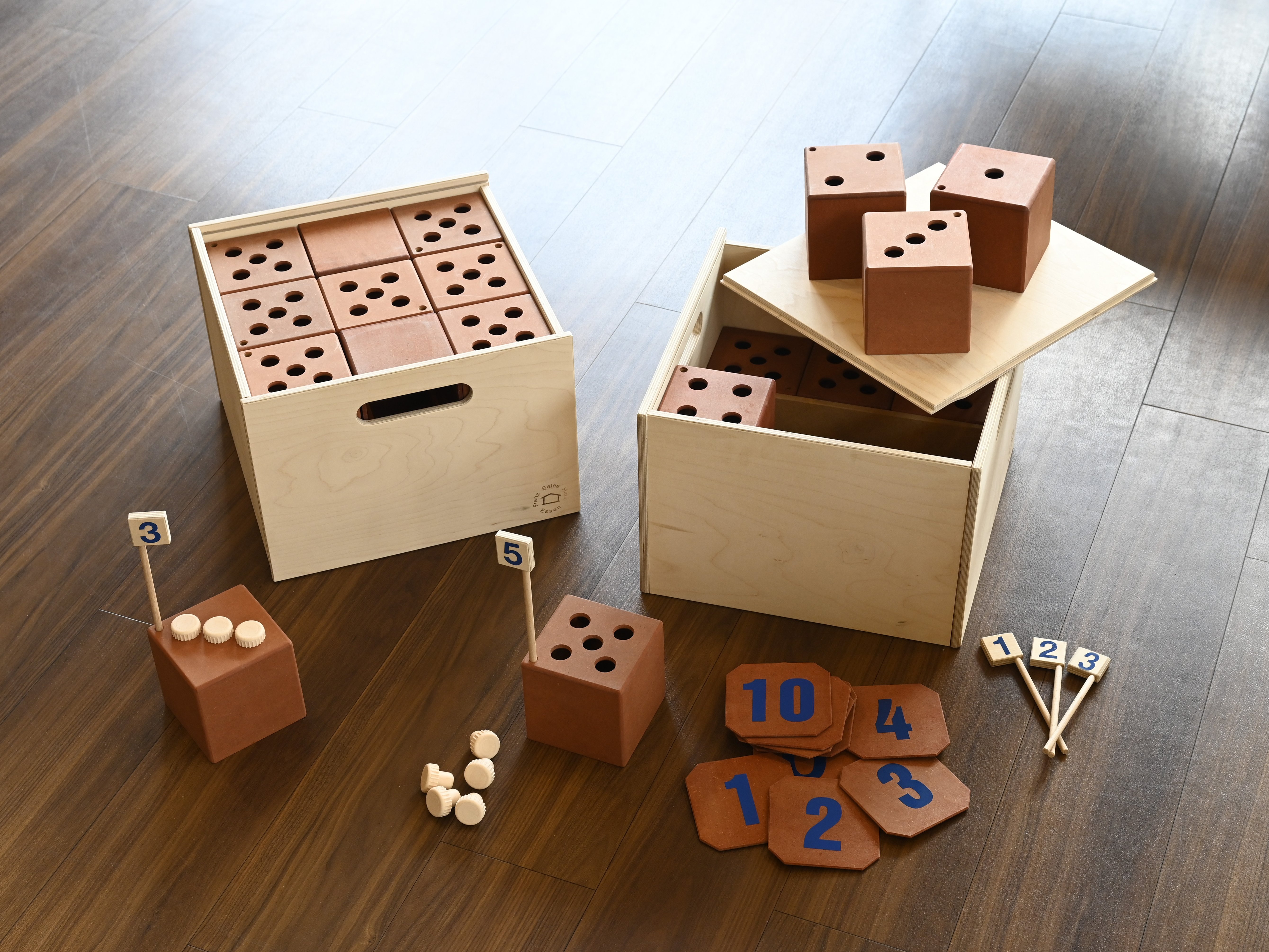 Holzkisten und Würfel mit Punkten, Zahlen und kleinen Bällen auf einem Holzboden.