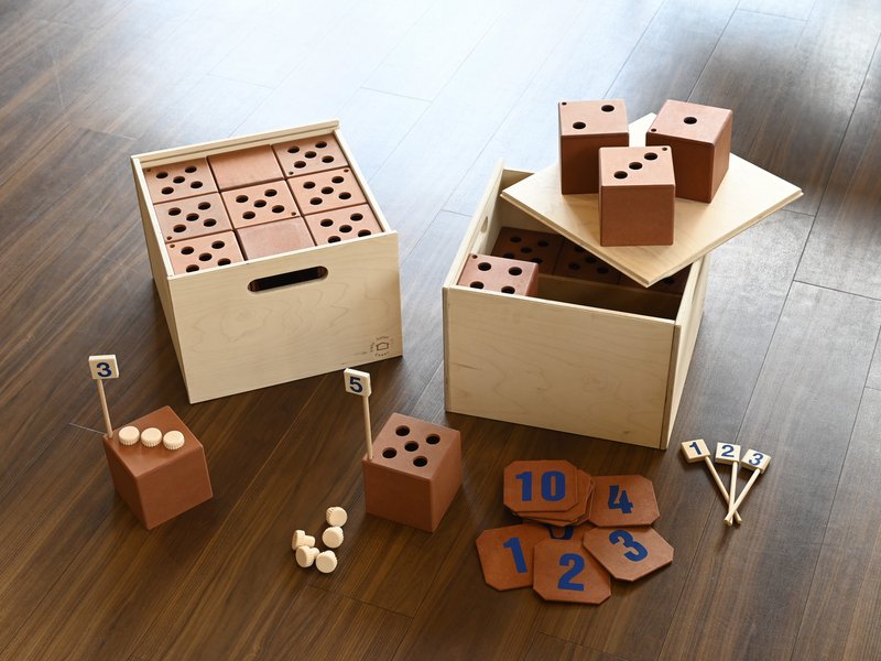 Holzkisten und Würfel mit Punkten, Zahlen und kleinen Bällen auf einem Holzboden.