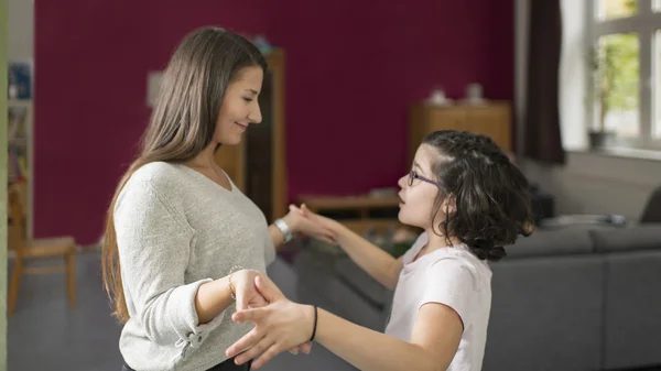 Zwei Personen tanzen freudig in einem Wohnzimmer vor einer dunkelroten Wand.