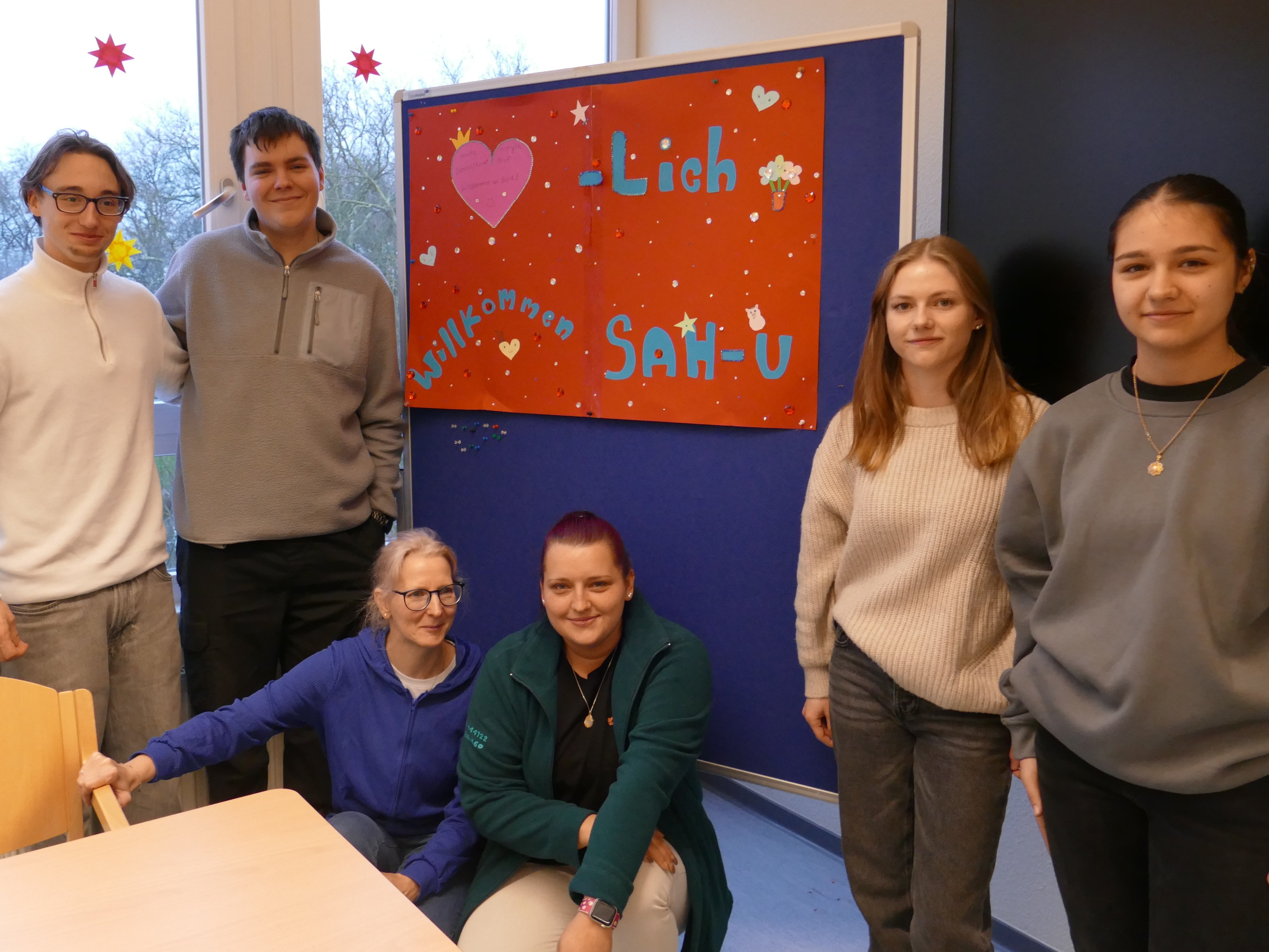 Schüler aus dem Oberkurs stehen vor einem Plakat mit der Aufschrift "Herzlich willkommen SAH-U". Damit ist der neue Unterkurs der Sozialassistenten gemeint.