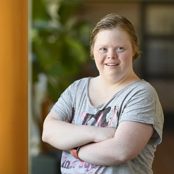 Person lächelt glücklich, stehend in Flur mit grünen Pflanzen im Hintergrund.