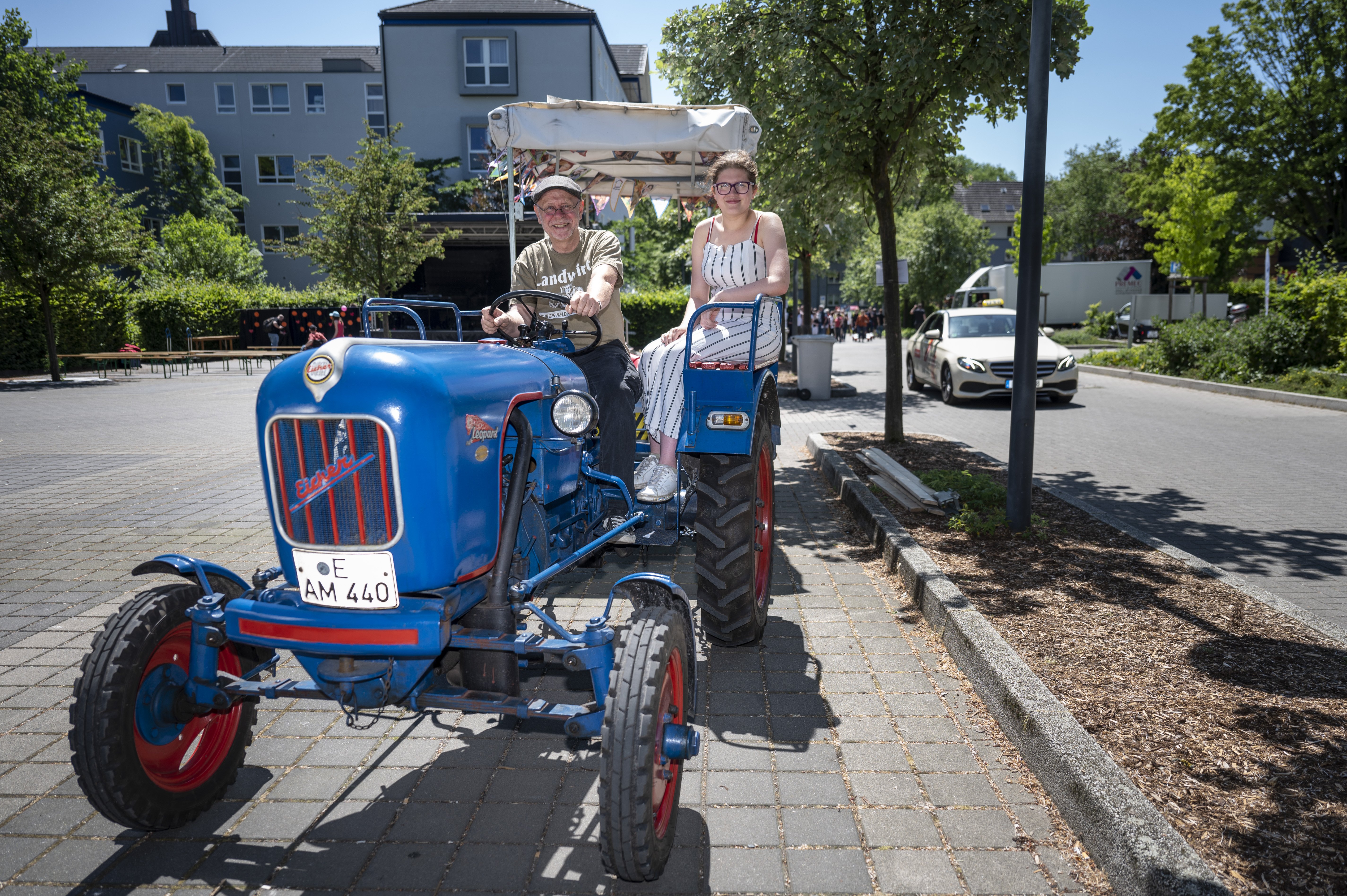 Auf einem blauen, älteren Trecker sitzen der Fahrer und an der Seite ein Mädchen.