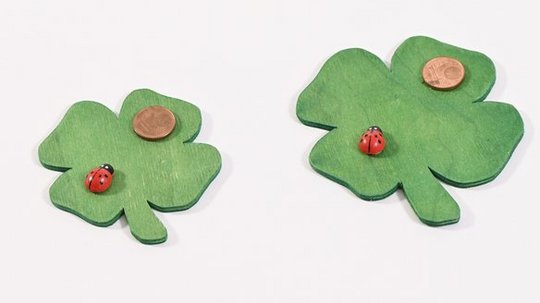 Zwei grüne Kleeblätter mit Marienkäfern und Kupfermünzen auf weißem Hintergrund.