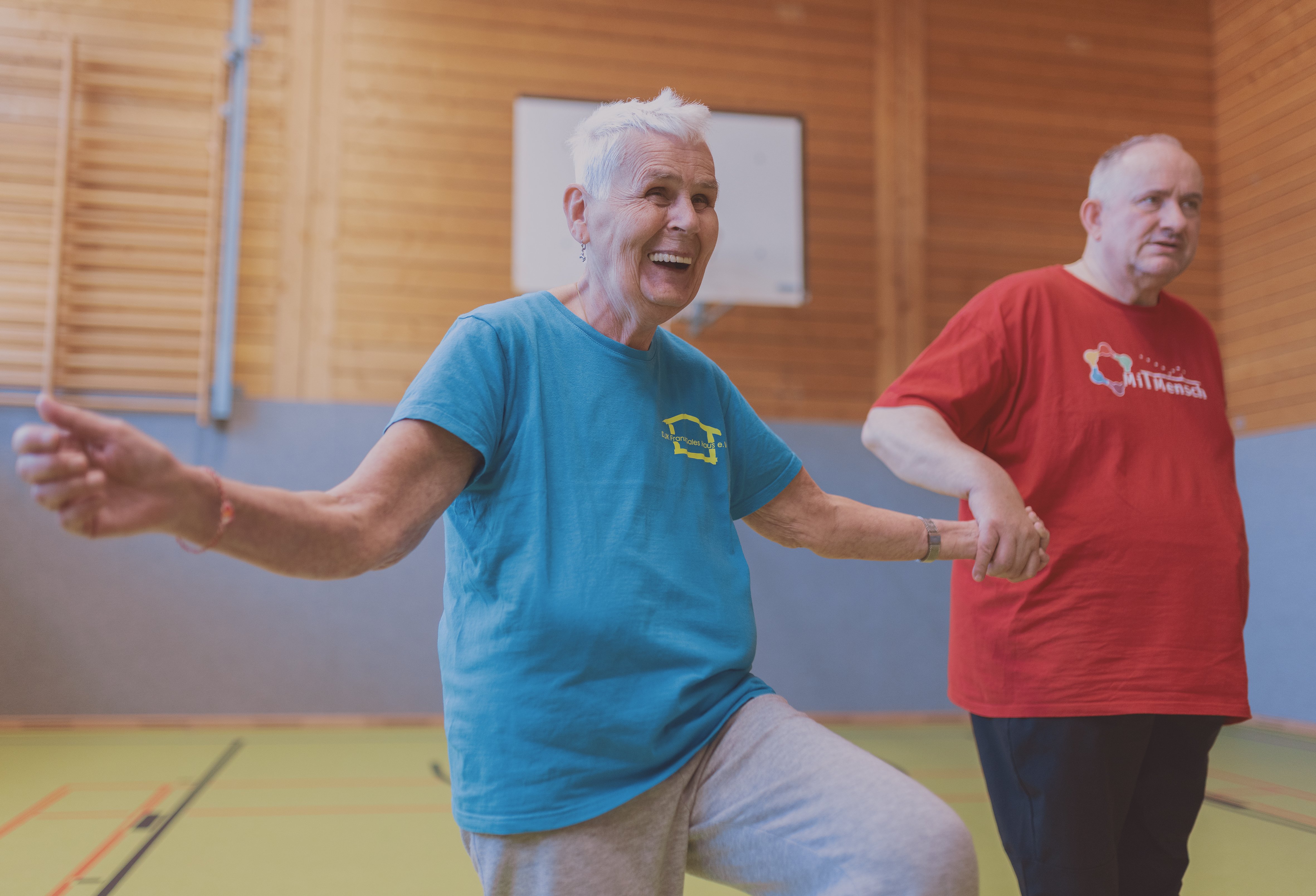 Zwei ältere Sportler, eine Frau und ein Mann, bei Übungen im Stehen.