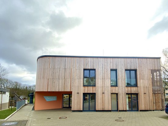 Eingang der Auszeit Bochum. Orangene Wand in einem modernen Gebäude aus Holz und Glas