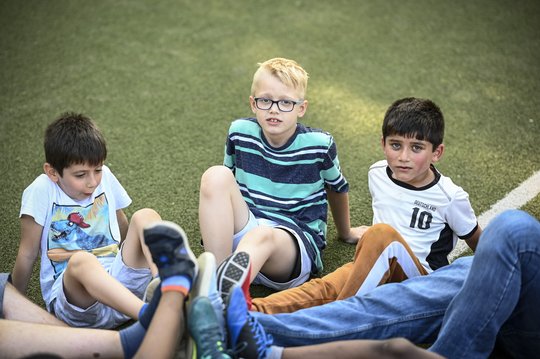 Kinder sitzen im Kreis und strecken beim Fußballtraining ein Bein aus, sodass sich die Füße in der Mitte berühren