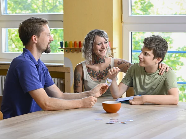 Familienhelferin sitzt mit Vater und Sohn am Esstisch.
