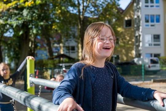 Ein lachendes Kind mit Brille auf einem Spielplatz bei sonnigem Wetter.