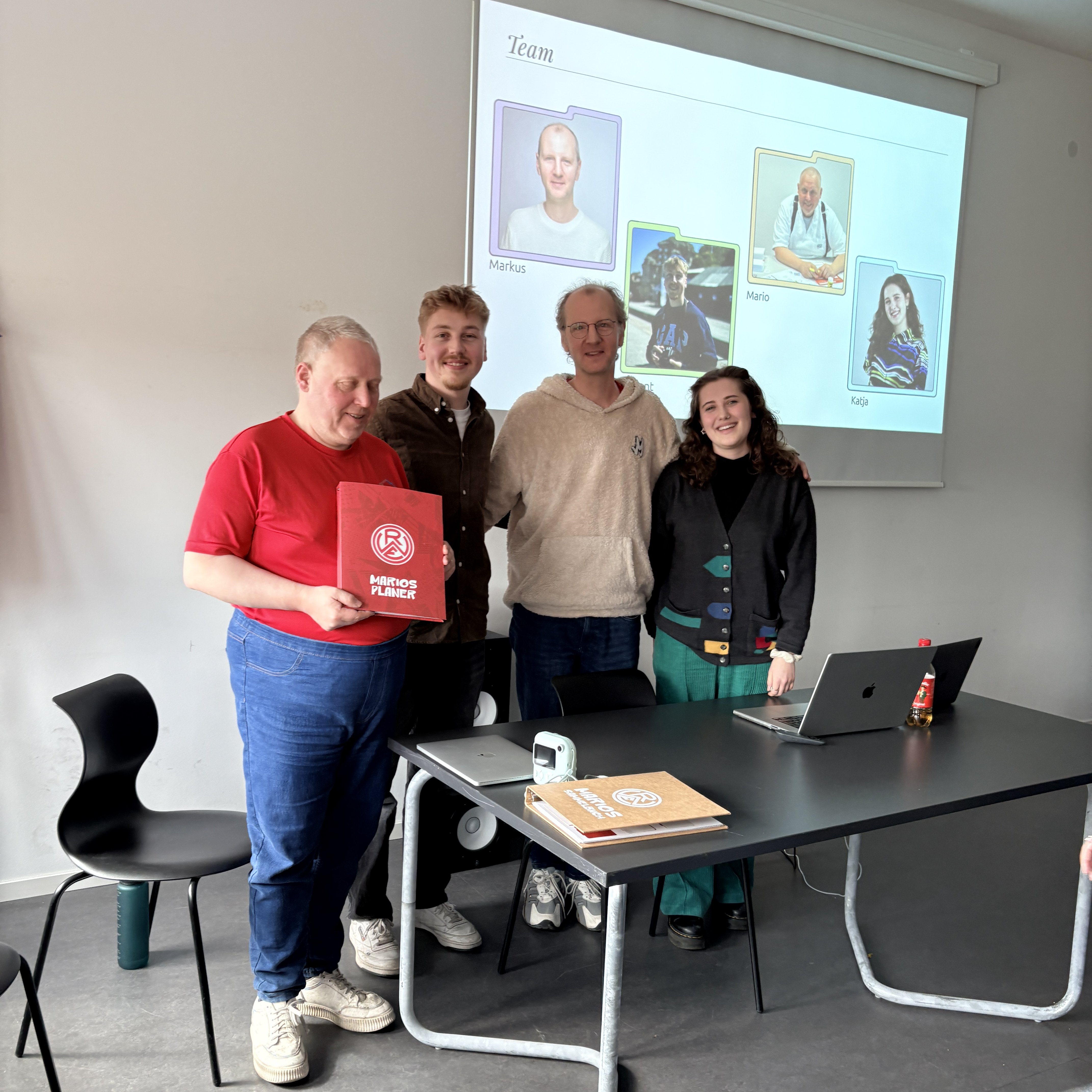 Zwei Design-Studierende und zwei Werkstatt-Beschäftigte stehen vor einen großen Bildschirm, auf dem eine Präsentation zu sehen ist.