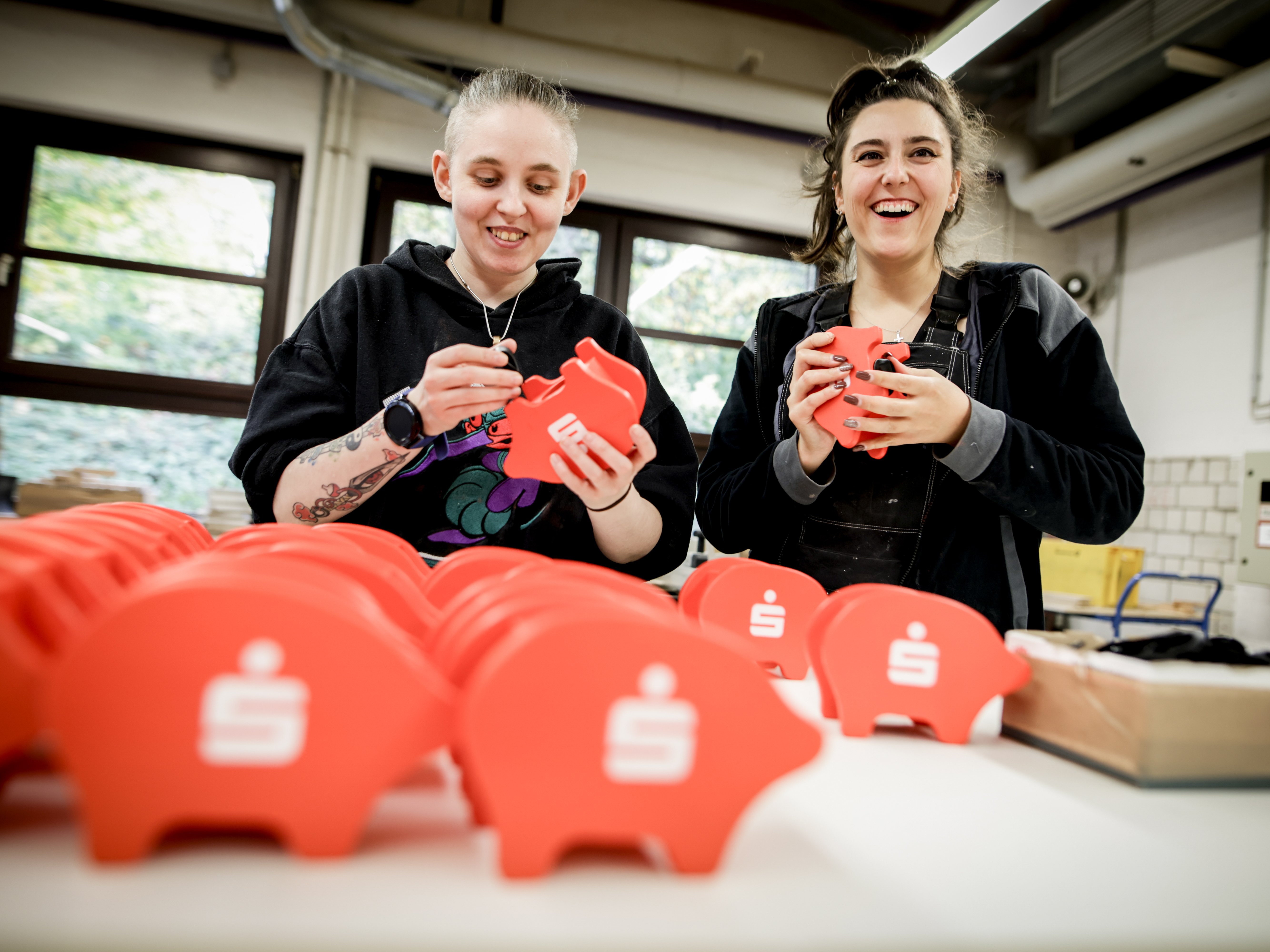 Zwei junge Frauen mit den roten Sparschweinen in der Hand und lachenden Gesichtern