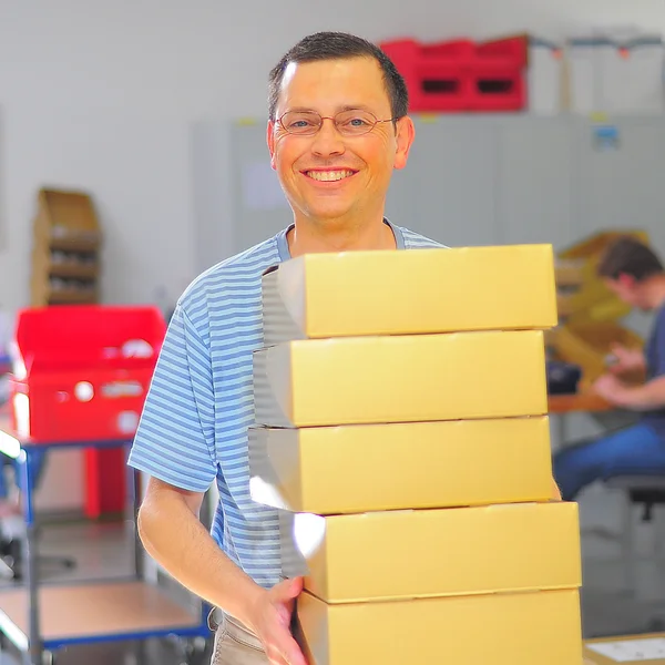 Lächelnder Mann trägt mehrere Kartons in seinen Arbeitsbereich