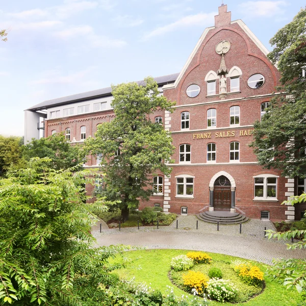 Fassade des Franz Sales Hauses mit Bäumen und Garten im Vordergrund.