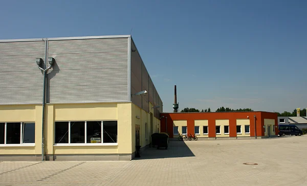 Industriegebäude bei sonnigem Wetter mit gepflastertem Vorplatz und klarem Himmel.