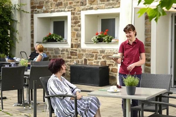 Frau bedient Gast auf einer Sonnenterrasse