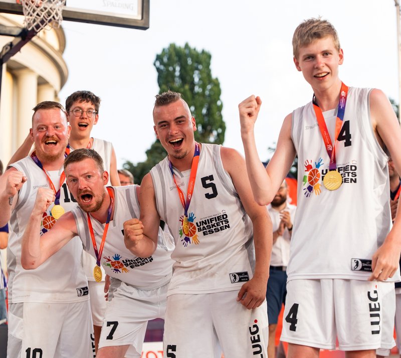 Fünf Basketball-Spieler jubeln in die Kamera. Sie haben Goldmedaillen um den Hals.