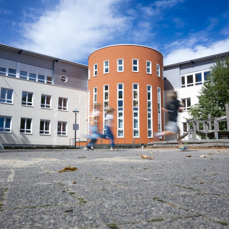Ansicht des Schulhofs im Sommer mit viel Asphalt vorne